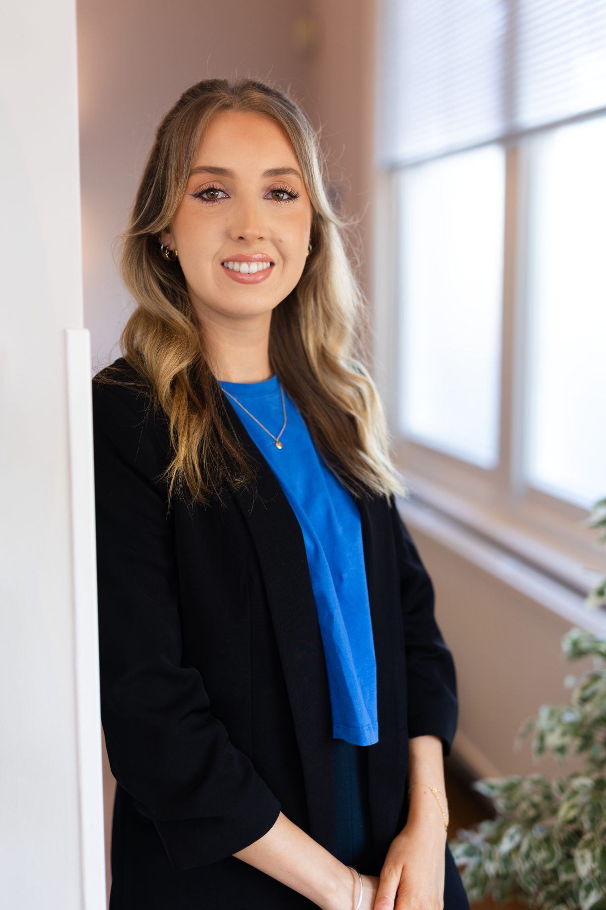 Reception team member Jenny Brugada smiling in the practice reception area, wearing a black blazer and blue top.