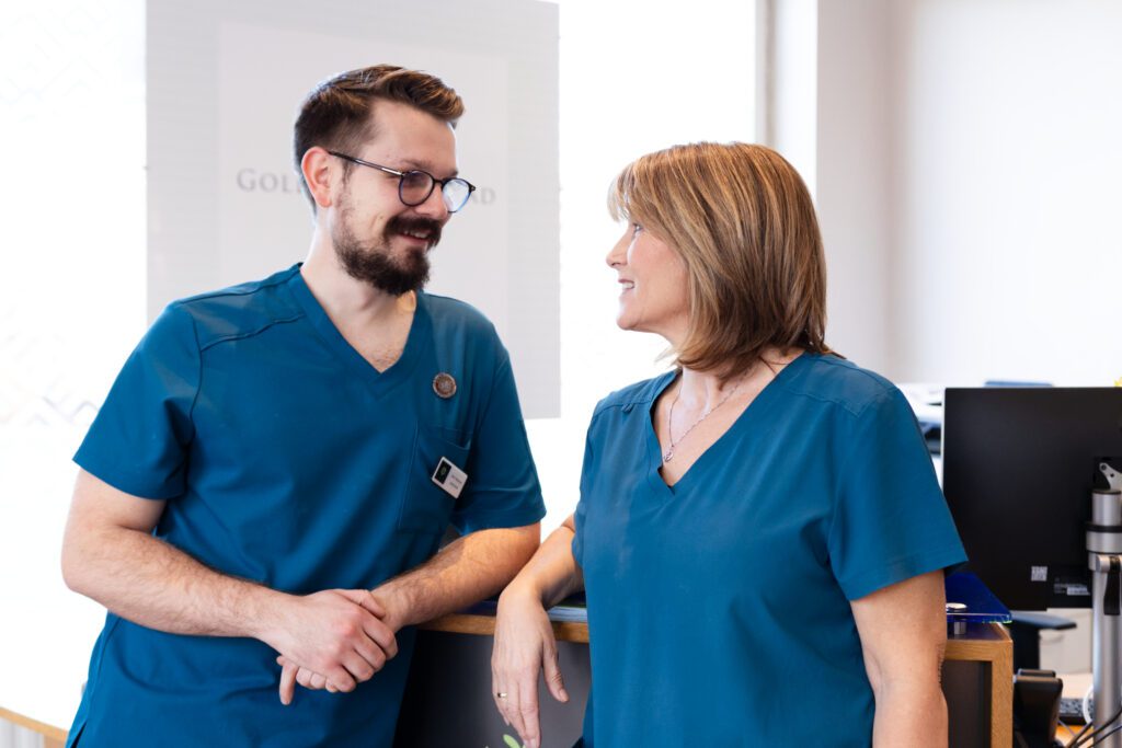Male and female dentist chatting and leaning on the reception desk