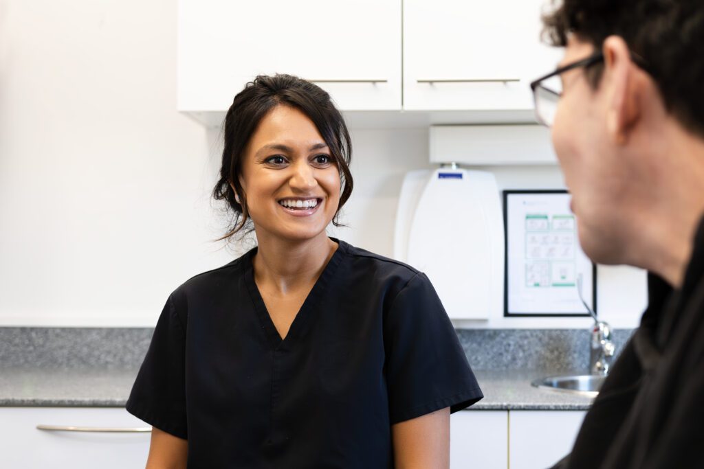Female dentist with brown hair smiling and looking at someone blurred at the side of the camera