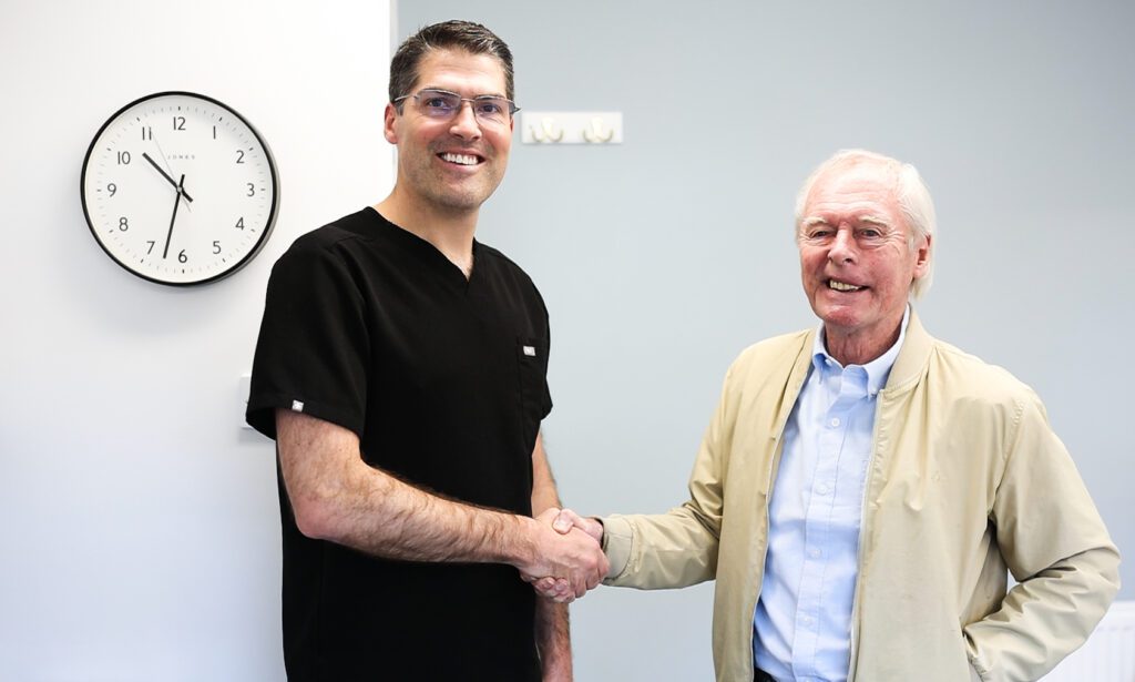 Male dentist shaking hands with a mature male patient both smiling at camera