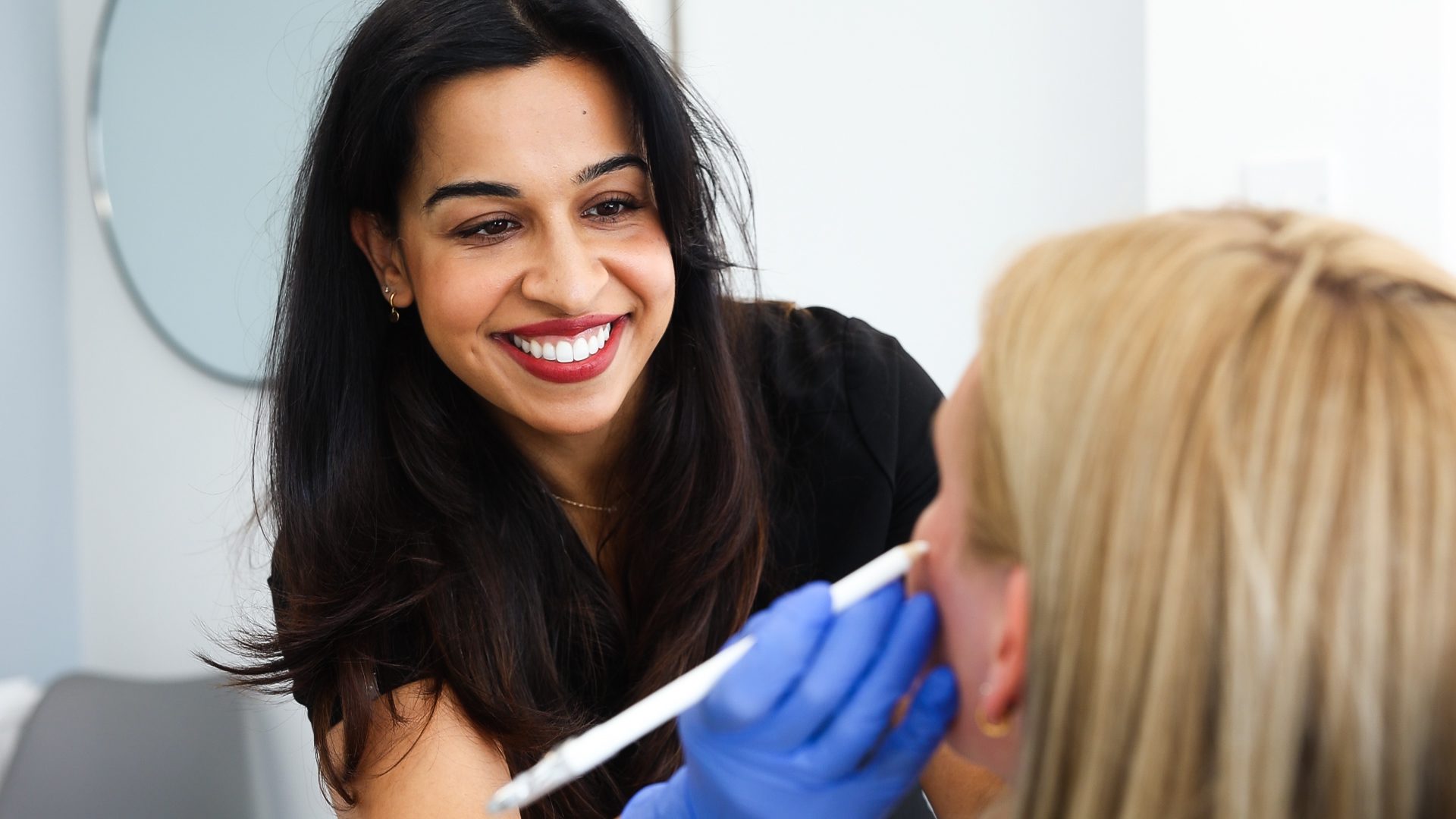 female dentist smiling at patient and holding a white pencil