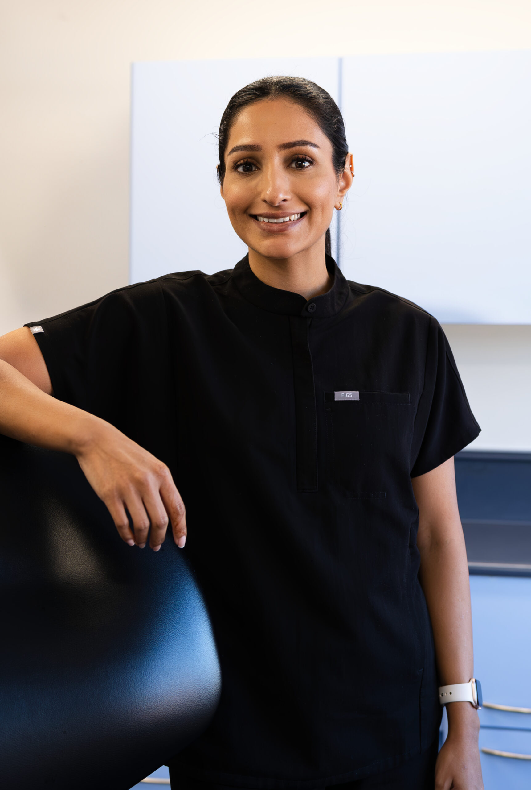 female dentist leaning on a dentist chair smiling