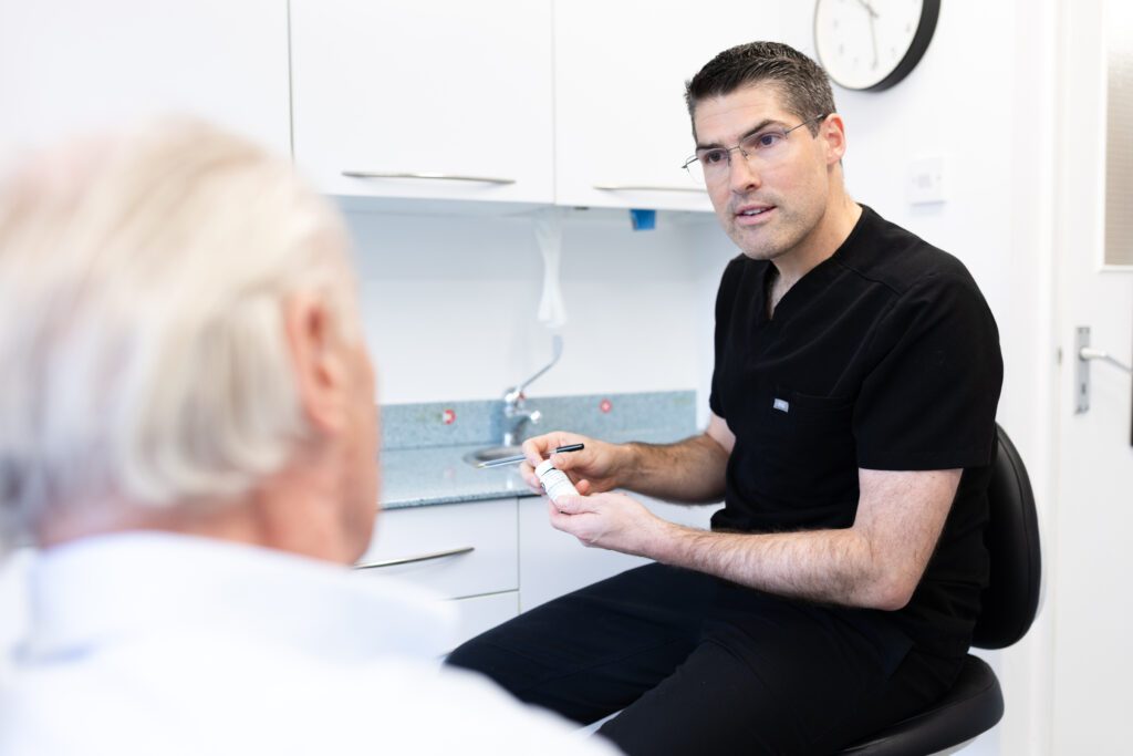 Male principle dentist talking to a patient and holding medicine and a pen